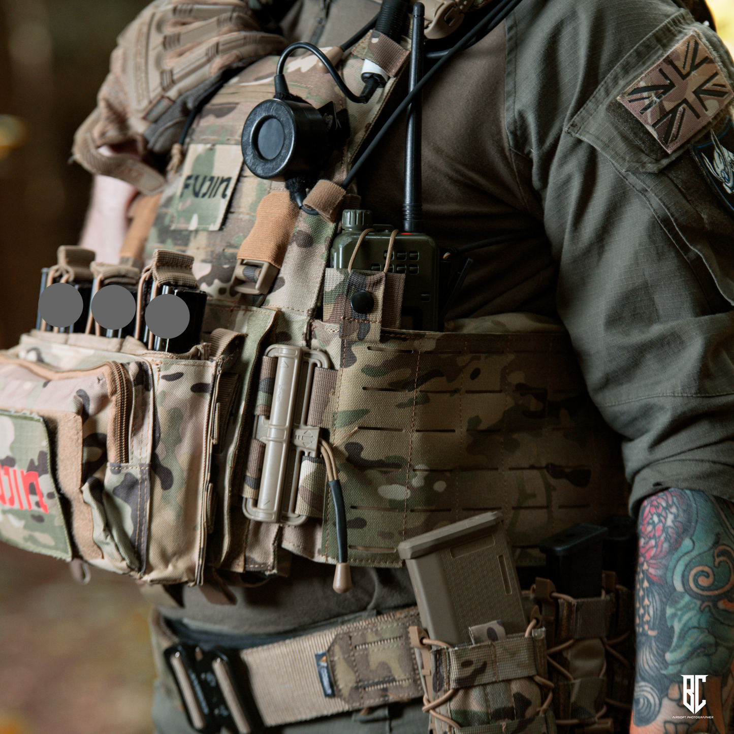 Person wearing a tactical vest with various equipment and a tattooed arm.