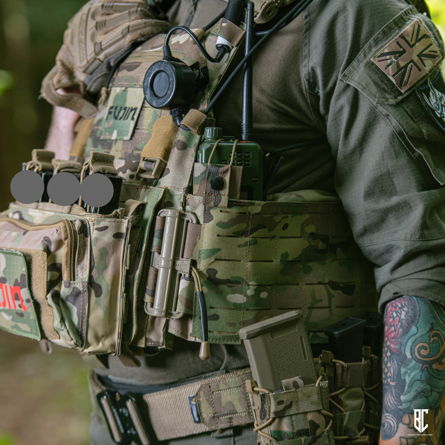 Person wearing a tactical vest with various equipment and British flag patch.